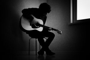 Man,Sitting,On,Stool,In,Dark,Room,Playing,Guitar